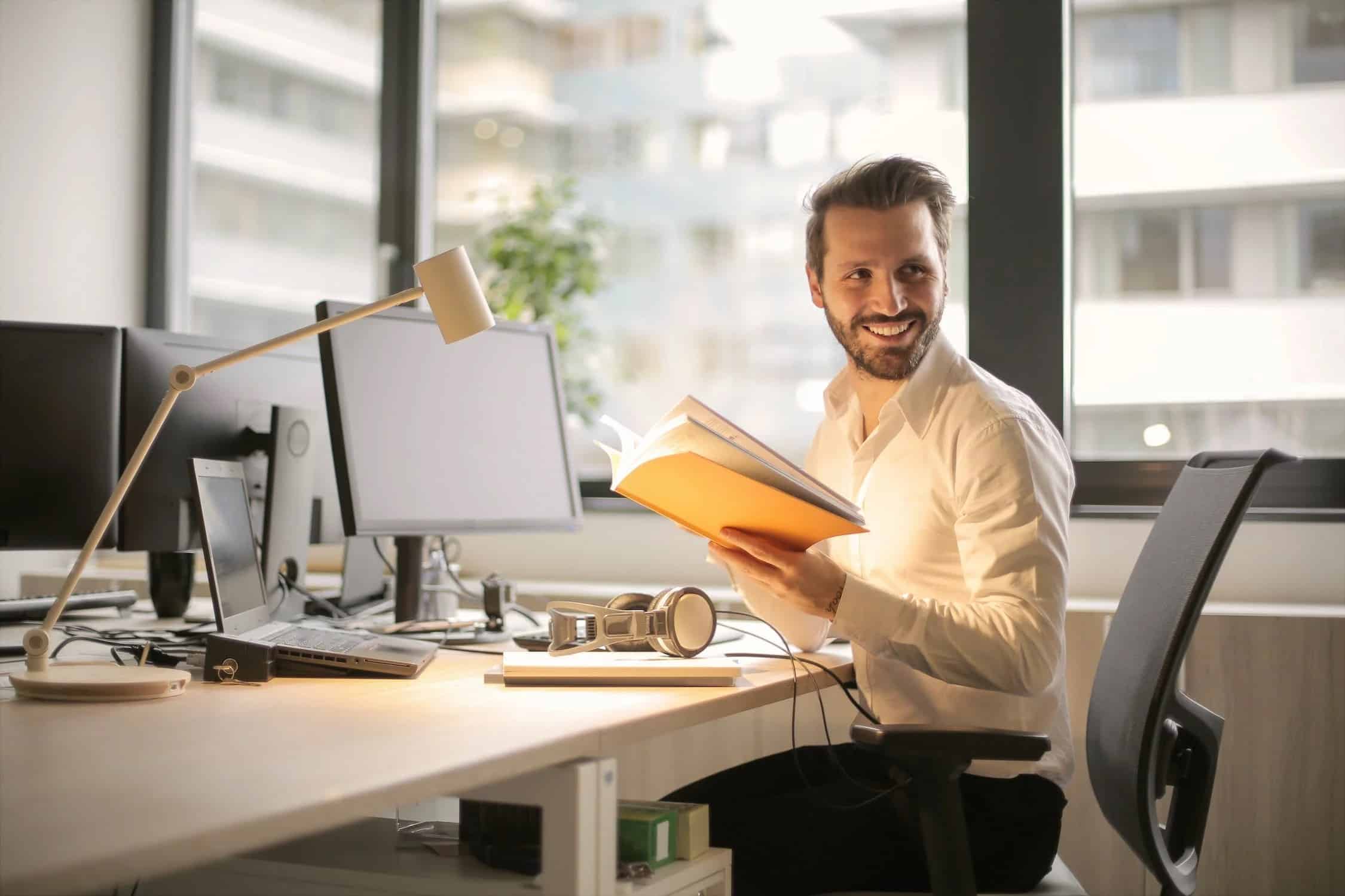 A smiling man in an office holding a notebook